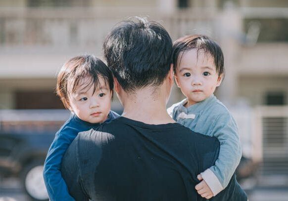 rear view asian chinese father carrying his twin baby boys walking back home in the morning from public park